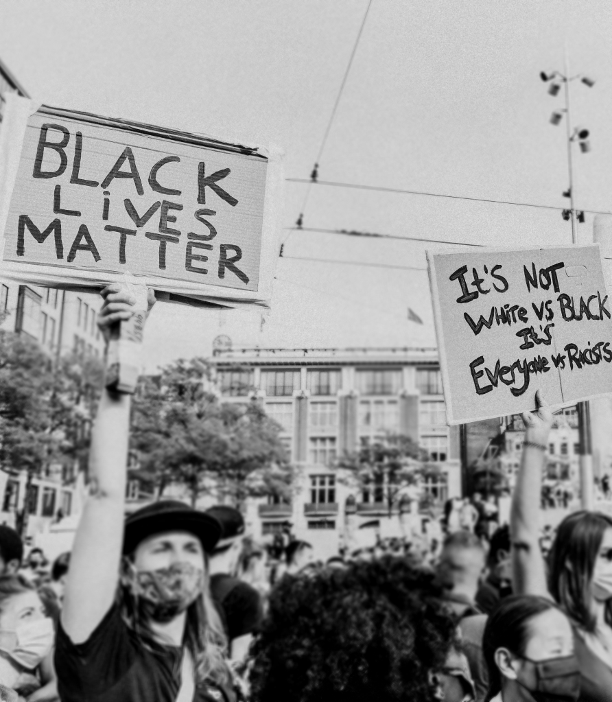 Photo of protesters holding signs saying Black Lives Matter and It's not White versus Black, it's everyone versus racists
